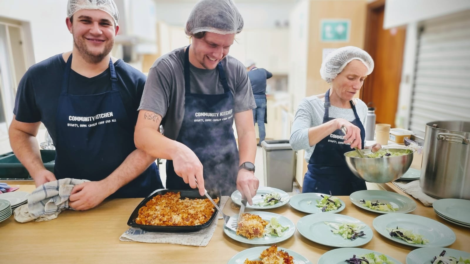 A photograph of three Community Kitchen chefs, plating up food and looking thrilled