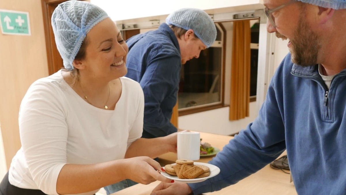 A delighted kitchen worker hands a member of hosting team a plate of biscuits