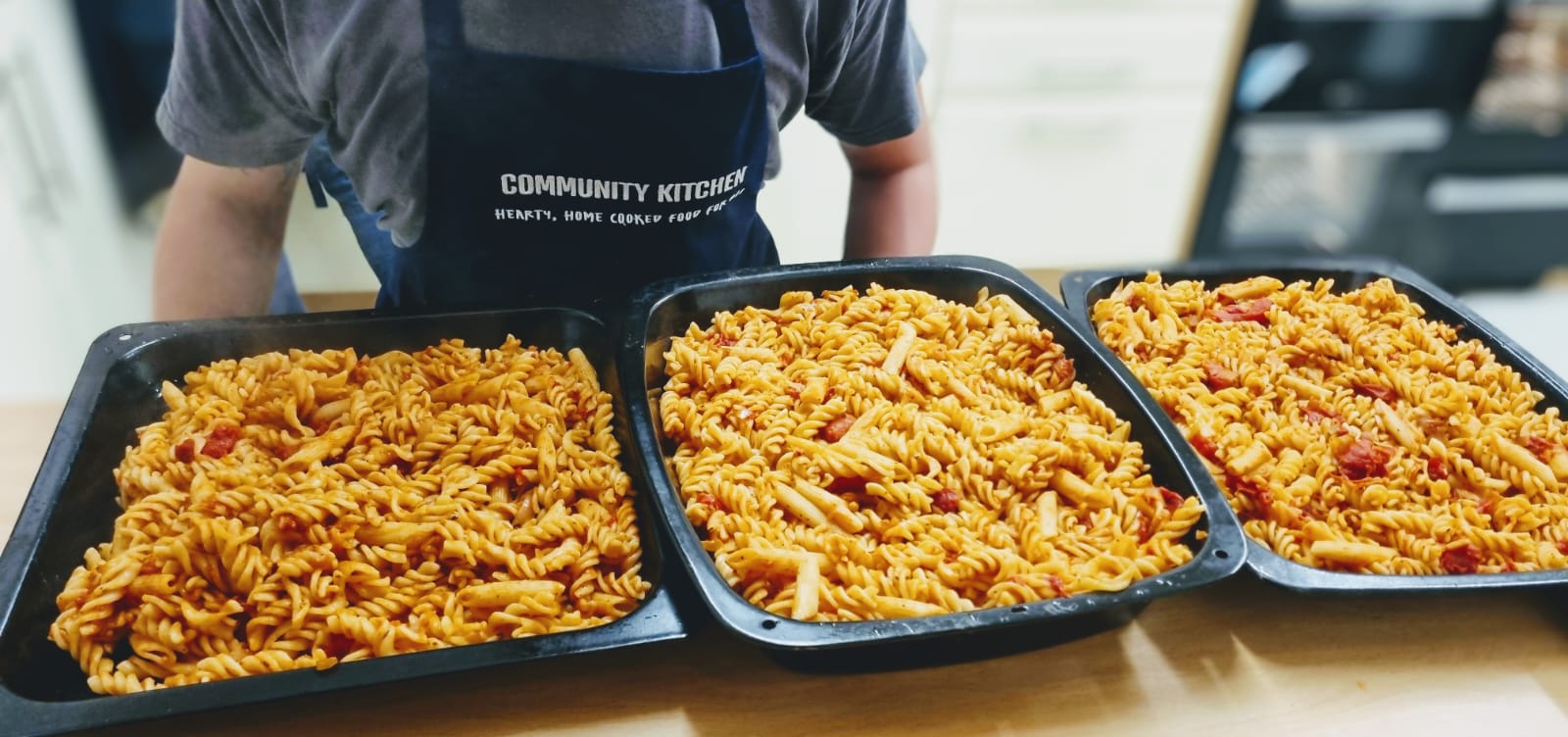 Three large baking trays of cooked tomato pasta bake